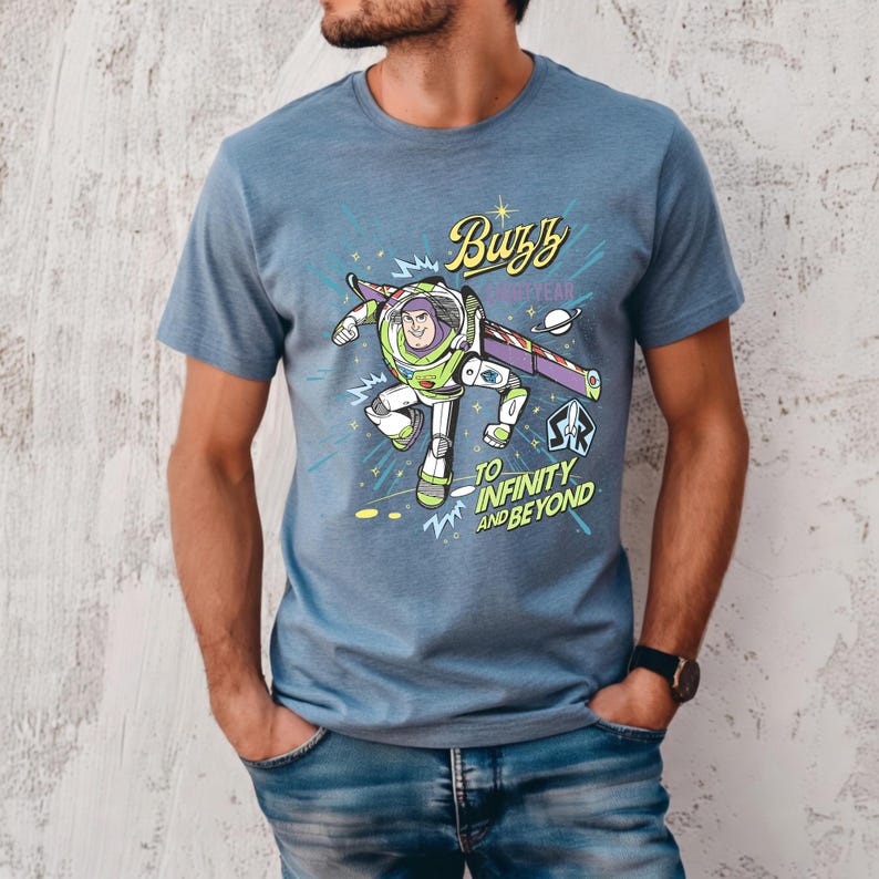 May include: Blue t-shirt featuring a graphic of Buzz Lightyear from Toy Story. The design includes the text "Buzz" and "To Infinity and Beyond" with a space-themed background. The shirt is made of a soft material.