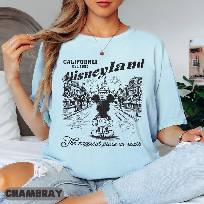May include: Light blue t-shirt with a black and white Disneyland graphic. The graphic features Mickey Mouse in front of a street scene with the text "California Est. 1955 Disneyland The happiest place on earth."