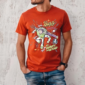 May include: A red t-shirt featuring a graphic of Buzz Lightyear from Toy Story. The design includes the text "Buzz Lightyear" and "To Infinity and Beyond" with a cartoon image of the character in action. The shirt is short-sleeved.