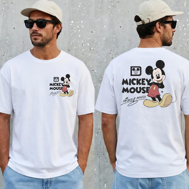 May include: White t-shirt featuring Mickey Mouse. The front of the shirt has a small graphic of Mickey Mouse with the words "Mickey Mouse" and a signature. The back of the shirt has a larger Mickey Mouse graphic and the words "Mickey Mouse".