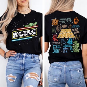 以下が含まれることがあります： 黒いTシャツ。ベビーヨーダのグラフィックと「May the 4th Be With You」の文字とライトセーバーのデザインが特徴です。Tシャツの背面にはスターウォーズをテーマにしたグラフィックとテキストがあります。青いジーンズと組み合わせています。