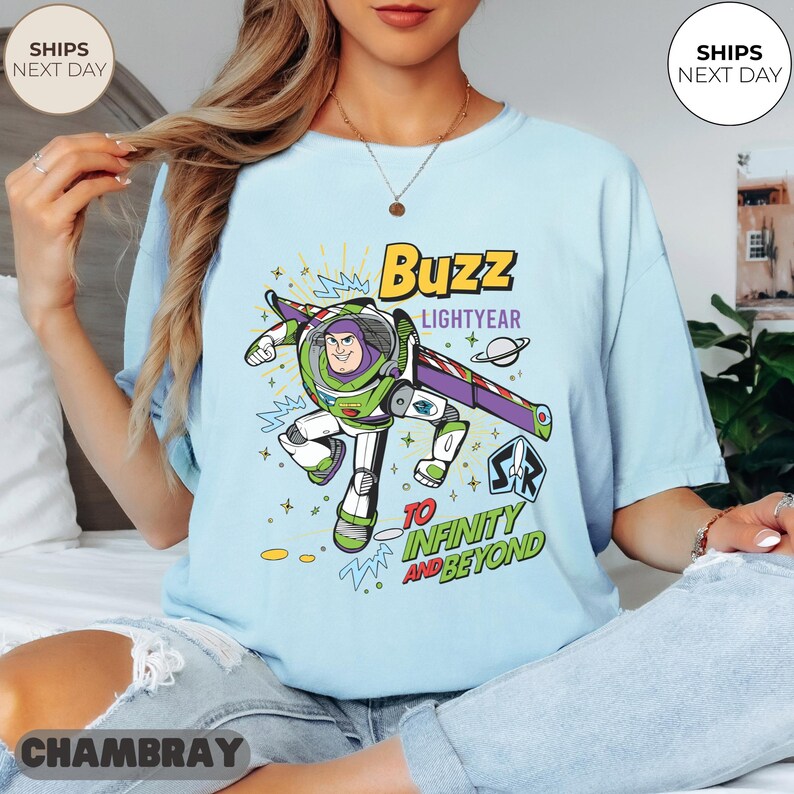 K&ouml;nnte beinhalten: Hellblaues T-Shirt mit einer Grafik von Buzz Lightyear aus Toy Story. Das Design enth&auml;lt den Text "Buzz Lightyear" und "To Infinity and Beyond". Das Shirt hat einen Rundhalsausschnitt und kurze &Auml;rmel.