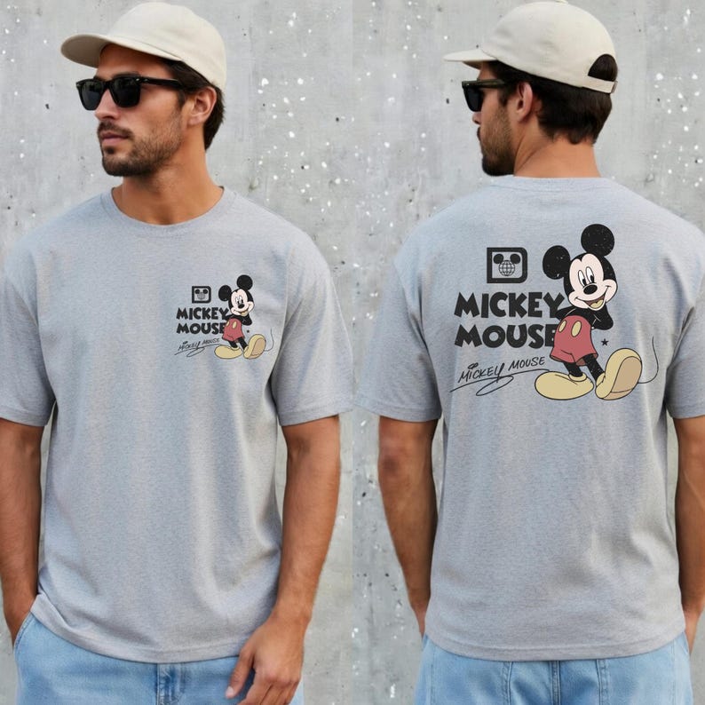 May include: A light gray t-shirt featuring Mickey Mouse. The front of the shirt has a small graphic of Mickey Mouse with the words "Mickey Mouse" and a signature. The back of the shirt has a larger Mickey Mouse graphic and the words "Mickey Mouse".
