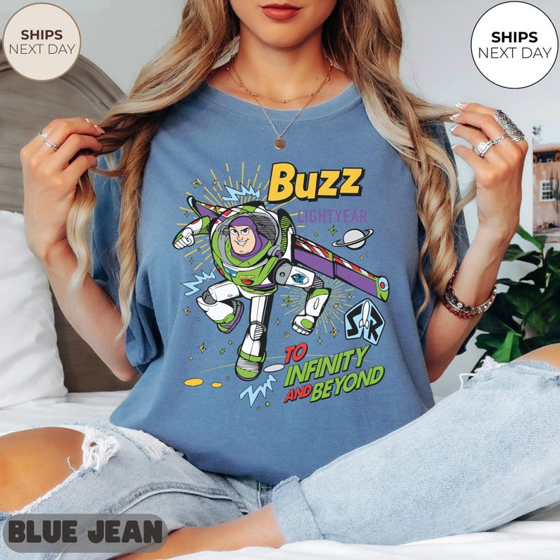 K&ouml;nnte beinhalten: Blaues T-Shirt mit einem Buzz Lightyear-Motiv, mit dem Text "Buzz Lightyear" und "To Infinity and Beyond". Das Design ist in Gr&uuml;n, Lila, Wei&szlig; und Gelb gehalten. Das T-Shirt hat eine lockere Passform.