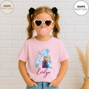 May include: A pink t-shirt with a graphic of the number 4, snowflakes, and the characters Anna and Elsa, with the name "Evelyn". The shirt is worn by a young girl wearing heart-shaped sunglasses and chewing bubblegum.