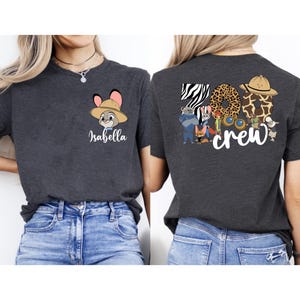 Puede incluir: Camiseta gris oscuro con un personaje de dibujos animados con sombrero de safari y el nombre "Isabella". La parte trasera de la camiseta muestra "Zoo Crew" con letras con estampado animal y varios personajes de dibujos animados.
