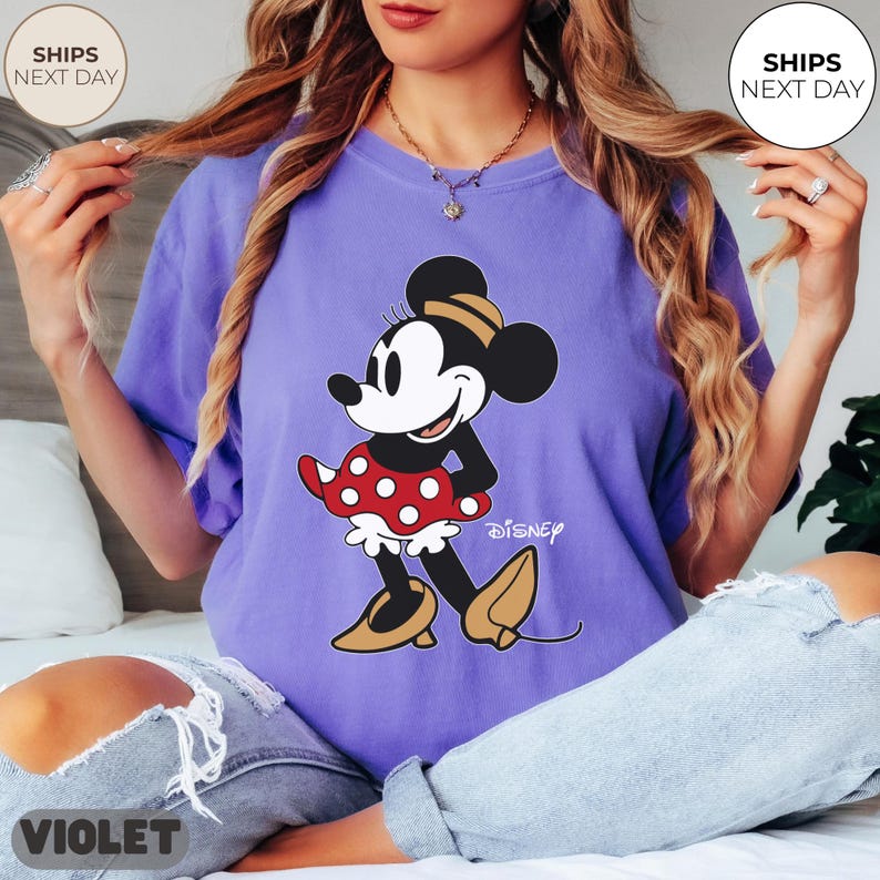 Puede incluir: Camiseta violeta con un gr&aacute;fico de Minnie Mouse. El gr&aacute;fico muestra a Minnie Mouse con una falda roja de lunares, una parte superior negra y zapatos amarillos. La palabra "Disney" est&aacute; impresa debajo. La camiseta tiene un corte holgado.