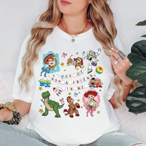 May include: White t-shirt with a colourful Toy Story design. The graphic includes cartoon characters such as Woody, Buzz Lightyear, and Slinky Dog, along with the text "You've Got a Friend in Me".
