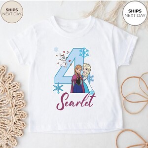 May include: White t-shirt with a blue number 4 design, snowflakes, and characters Anna, Elsa, and Olaf from Frozen. The name "Scarlet" is written in a cursive font. The shirt has short sleeves.
