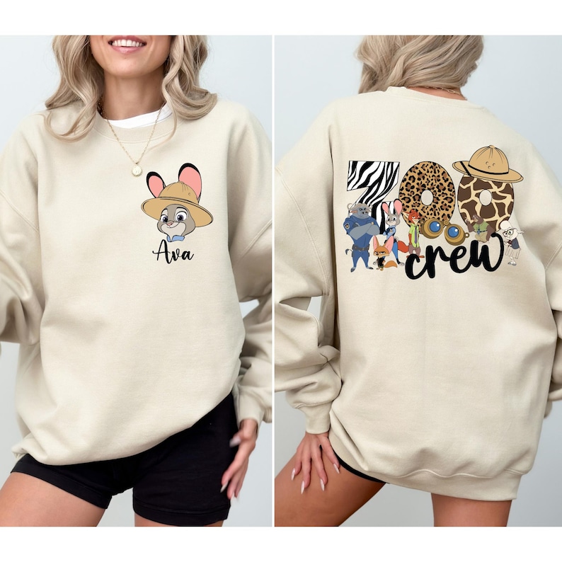 Puede incluir: Sudadera beige con un personaje de dibujos animados con sombrero y el nombre "Ava" debajo. La parte trasera de la sudadera tiene las palabras "Zoo Crew" con dise&ntilde;os de estampado animal y personajes de dibujos animados.