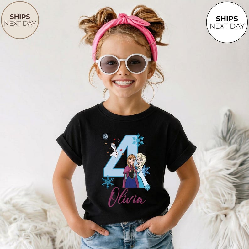 May include: Black t-shirt with a blue number 4, featuring cartoon characters Anna and Elsa from Frozen. The name "Olivia" is written below in cursive. The shirt is designed for a child's birthday celebration.