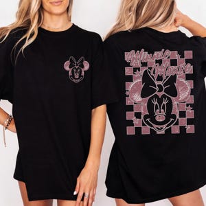 May include: Black t-shirts featuring a Minnie Mouse graphic. The front of the shirt has a small Minnie Mouse design, while the back showcases a larger design with the words "Minnie Mouse" and a checkered pattern.
