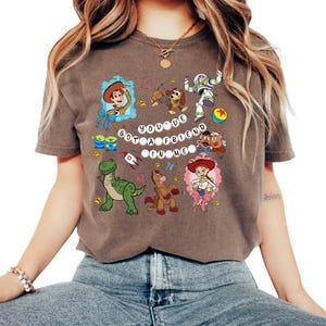 May include: A brown t-shirt with a vibrant graphic of Toy Story characters. The design includes Woody, Buzz Lightyear, and other characters, with the text "You've Got a Friend in Me".