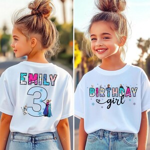 May include: White t-shirts with colorful graphics. One shirt has the name "EMILY" and the number "3" with cartoon characters. The other shirt says "BIRTHDAY girl" with snowflake and heart accents. Both shirts are worn by young girls.