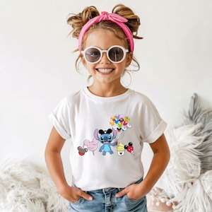 Puede incluir: Camiseta blanca con un dibujo animado de Stitch de Lilo & Stitch. El personaje azul sostiene globos, algod&oacute;n de az&uacute;car y conos de helado. La camiseta la lleva una persona joven. El gr&aacute;fico es colorido y llamativo.