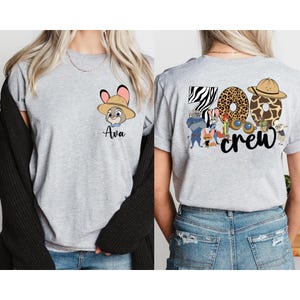 Puede incluir: Camiseta gris claro con un conejo de dibujos animados con sombrero de safari y el nombre "Ava". La parte trasera de la camiseta muestra el texto "Zoo Crew" con dise&ntilde;os de estampado animal y personajes de dibujos animados.