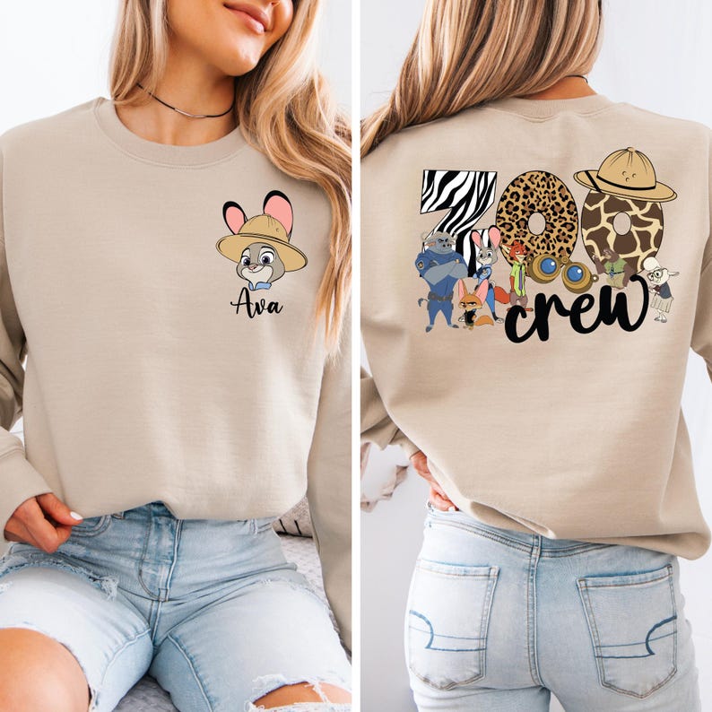 Puede incluir: Sudadera beige con un conejo de dibujos animados con sombrero y el nombre "Ava". La parte trasera tiene "Zoo Crew" con estampados de animales y personajes de dibujos animados. Una parte superior informal y divertida.