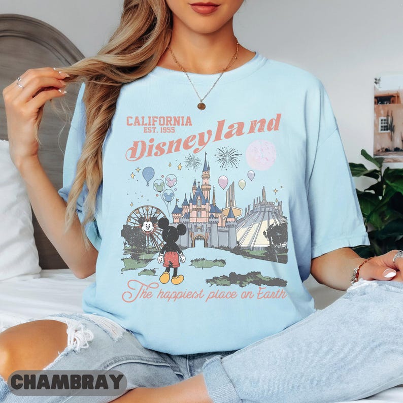 May include: Light blue t-shirt with a Disneyland graphic. The graphic features Mickey Mouse, a Ferris wheel, a castle, and the text "California Disneyland Est. 1955" and "The happiest place on Earth."