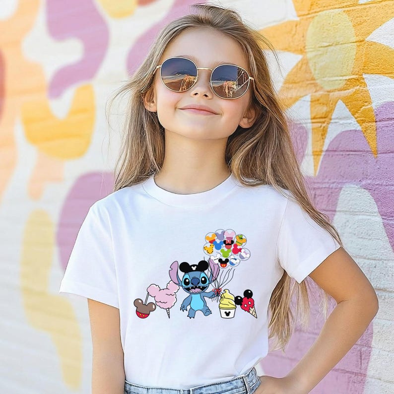 Puede incluir: Una camiseta blanca con un personaje de dibujos animados sosteniendo globos y golosinas. El personaje es azul con orejas grandes y un sombrero negro. La camiseta la lleva una persona con pelo largo y rubio y gafas de sol redondas.