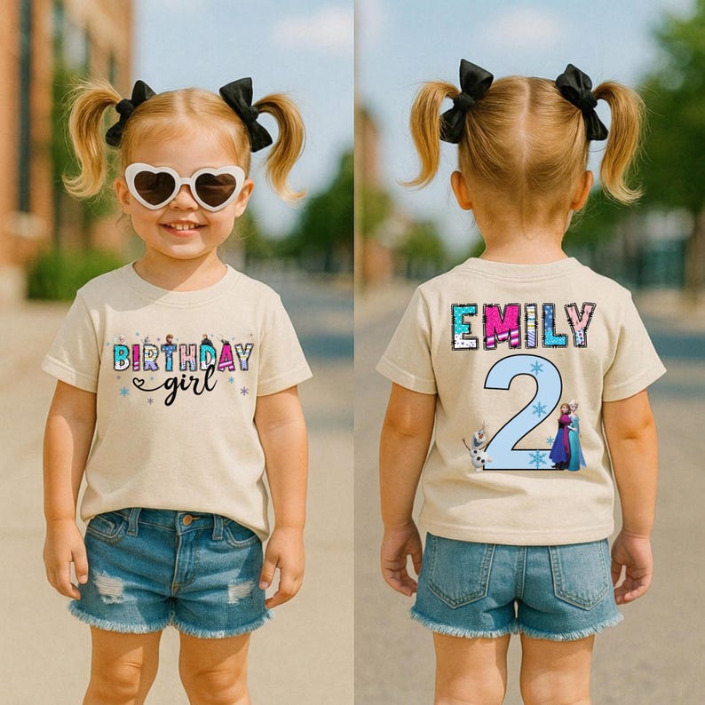 May include: A tan t-shirt with the text "Birthday girl" and a graphic of characters. The back of the shirt has the name "Emily" and the number "2" with cartoon characters. The child is wearing denim shorts.