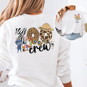 Puede incluir: Sudadera blanca con la inscripci&oacute;n "Zoo Crew" y gr&aacute;ficos con tem&aacute;tica animal. El dise&ntilde;o incluye una "Z" con estampado de cebra, una "O" con estampado de leopardo y una "O" con estampado de jirafa. La sudadera tambi&eacute;n tiene un peque&ntilde;o gr&aacute;fico en la parte delantera.