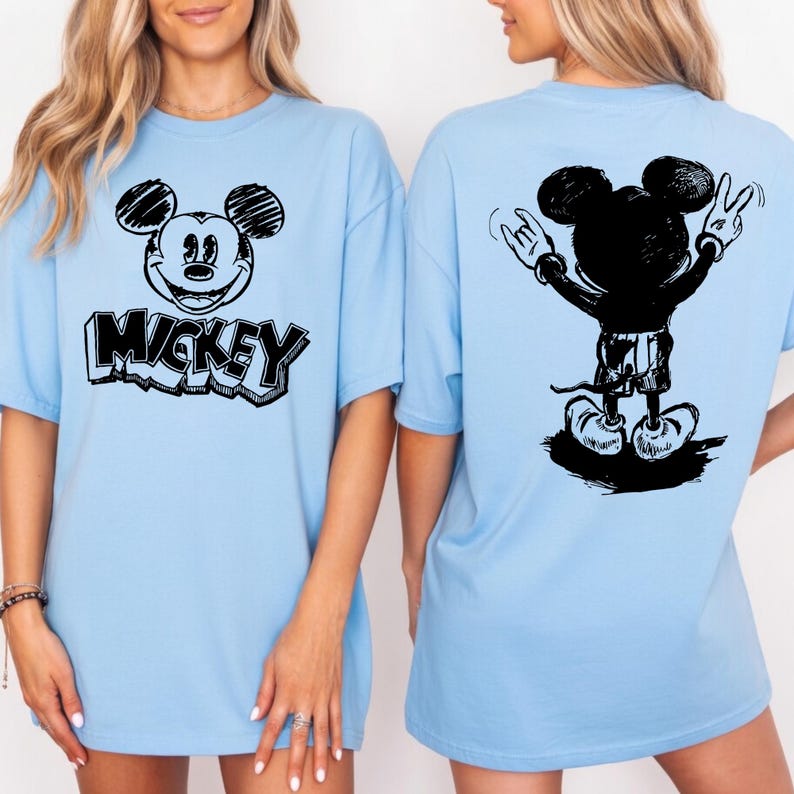 May include: Light blue t-shirts featuring a black and white Mickey Mouse design. The front of the shirt displays Mickey's face with the name "Mickey" below. The back of the shirt shows a silhouette of Mickey Mouse with his arms raised in a peace sign.
