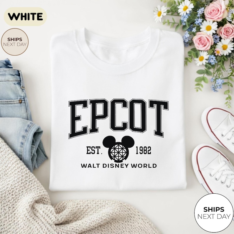 May include: White crew neck t-shirt with the word "EPCOT" in black block letters. Below the word "EPCOT" is "EST. 1982" and a Mickey Mouse head graphic. The text "WALT DISNEY WORLD" is below the graphic.