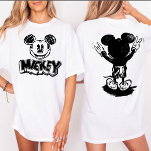 May include: White t-shirt featuring a black and white sketch of Mickey Mouse on the front with the word "Mickey" below. The back of the shirt shows a black silhouette of Mickey Mouse with his arms raised in a rock and roll gesture.