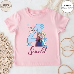 May include: A pale pink t-shirt with a blue number 4, snowflakes, and the Frozen characters Anna and Elsa. The name "Scarlet" is written in a cursive font below the number.