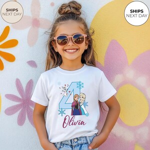 May include: A white t-shirt with a blue number 4 design, snowflakes, and characters from the film Frozen. The name "Olivia" is written in cursive. The girl is wearing pink sunglasses. The background is a colorful wall.