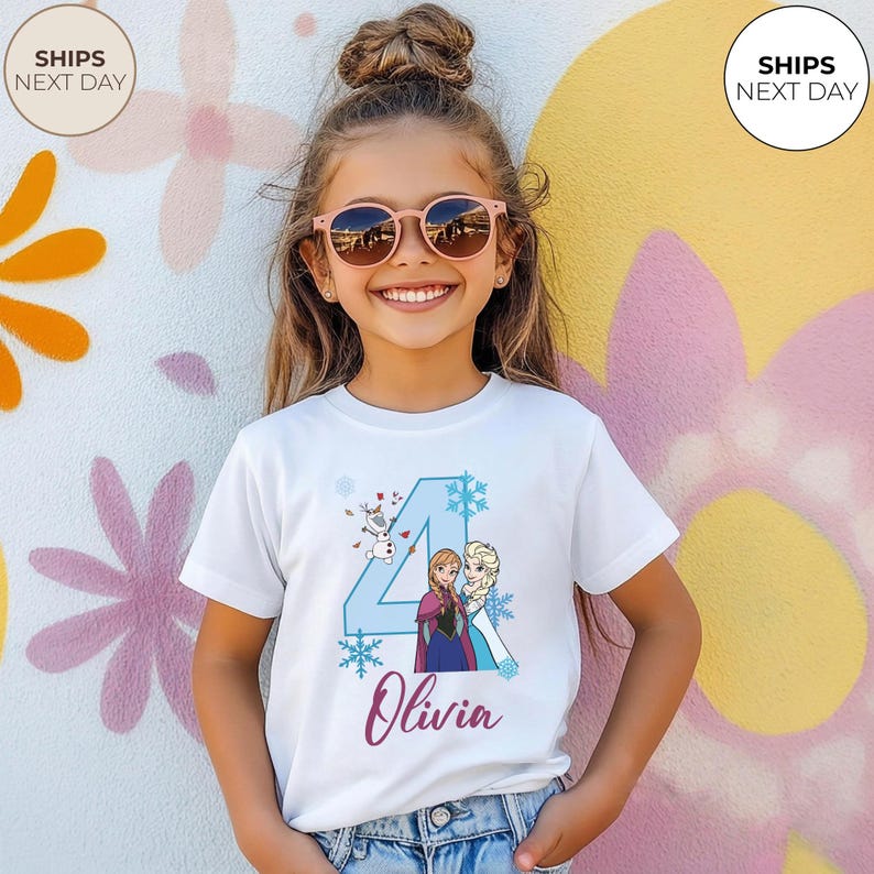 May include: A white t-shirt with a blue number 4 design, snowflakes, and characters from the film Frozen. The name "Olivia" is written in cursive. The girl is wearing pink sunglasses. The background is a colorful wall.