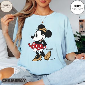 Puede incluir: Camiseta azul claro con un gr&aacute;fico de Minnie Mouse. El personaje de dibujos animados est&aacute; representado en negro, blanco, rojo y amarillo, con el logotipo de Disney. La camiseta es de estilo casual.
