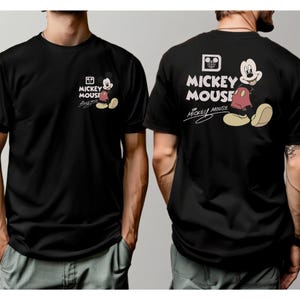 May include: Black t-shirt featuring Mickey Mouse. The front displays a small Mickey Mouse graphic with the words "Mickey Mouse" and signature. The back has a larger Mickey Mouse graphic with the words "Mickey Mouse" in white.