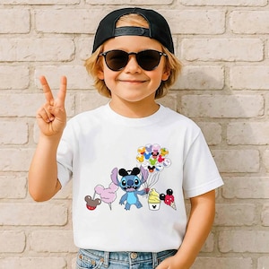 Puede incluir: Camiseta blanca con un personaje de dibujos animados sosteniendo globos, helado y algod&oacute;n de az&uacute;car. El personaje es azul con orejas grandes y un sombrero negro. La camiseta la lleva una persona con gafas de sol y una gorra negra.