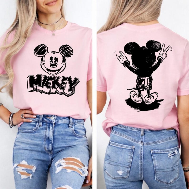 May include: A light pink t-shirt featuring a black and white graphic of Mickey Mouse on the front and back. The front design includes the word "Mickey" in a bold font. The back shows Mickey Mouse with his hands up in a rock and roll gesture.