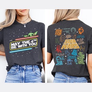 以下が含まれることがあります： スターウォーズをテーマにした濃いグレーのTシャツ。前面には、ライトセーバーとグローグーのグラフィックで「May the 4th Be With You」と表示されています。背面には、さまざまなスターウォーズのキャラクターと引用句が表示されています。