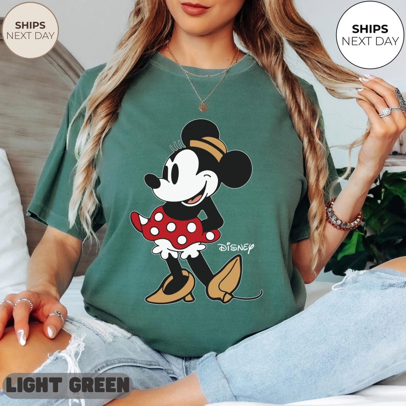 Puede incluir: Camiseta verde claro con un gr&aacute;fico de Minnie Mouse. El personaje lleva una falda roja de lunares y zapatos amarillos. La palabra "Disney" est&aacute; impresa debajo. La camiseta es de color liso y tiene un corte holgado.