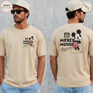 May include: Tan t-shirt featuring Mickey Mouse. The front has a small graphic of Mickey Mouse with the text "Mickey Mouse". The back has a larger Mickey Mouse graphic and the text "Mickey Mouse".