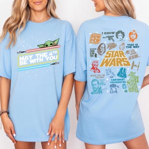 以下が含まれることがあります： ベビーヨーダ、ライトセーバー、そして「May the 4th Be With You」のテキストが特徴のライトブルーTシャツ。Tシャツの背面にはスターウォーズのキャラクターと引用句が描かれています。スターウォーズファン向けのカジュアルなTシャツです。