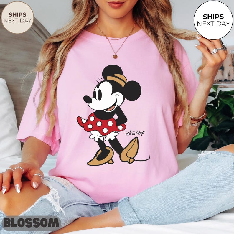 Puede incluir: Camiseta rosa claro con un dibujo de Minnie Mouse. Minnie se representa en una pose cl&aacute;sica, con una falda roja de lunares, zapatos amarillos y un lazo a juego. El logotipo de Disney est&aacute; impreso debajo.
