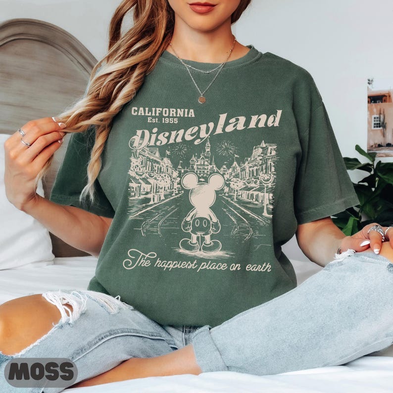 May include: Green t-shirt with a Disneyland graphic. The graphic features Mickey Mouse, a street scene, and the text "CALIFORNIA Est. 1955 Disneyland The happiest place on earth."