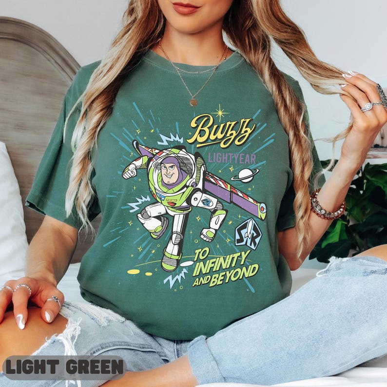 Może przedstawiać: Jasnozielona koszulka z grafiką Buzza Astrala, napisem "Buzz Lightyear" i "To Infinity and Beyond". Projekt zawiera statek kosmiczny i planetę. Koszulka ma okrągły dekolt.