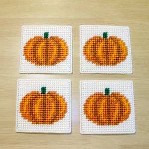 May include: Four white square coasters with a stitched design of orange pumpkins with green stems.
