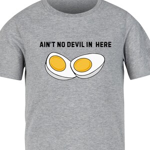Könnte beinhalten: Ein graues T-Shirt mit dem Text "Ain't no devil in here" und einer Grafik von zwei halbierten gekochten Eiern.