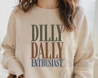 May include: A beige sweatshirt with the words "DILLY DALLY ENTHUSIAST" printed in green, brown, and blue. The sweatshirt has a crew neck and long sleeves.