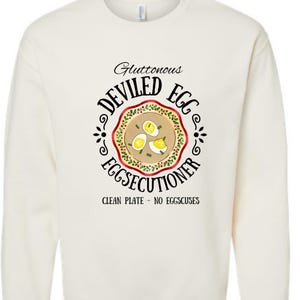 May include: A white long-sleeved shirt with a black and red graphic of a plate of deviled eggs. The graphic says "Gluttonous Deviled Egg Eggsecutioner" and "Clean Plate - No Eggscuses".