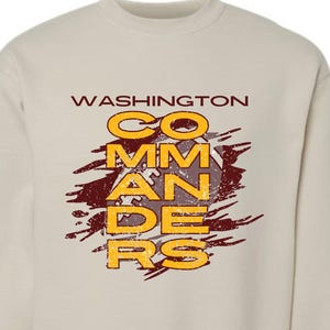 May include: A beige long-sleeve sweatshirt with the text "WASHINGTON COMMANDERS" in a distressed, layered font. The text is in yellow and maroon with a football graphic in the center.