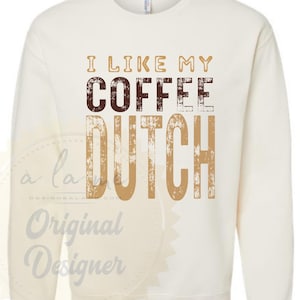 Puede incluir: Sudadera de color crema con el texto "I LIKE MY COFFEE DUTCH" en letras de bloque marrones y beige. La sudadera tiene cuello redondo y mangas largas. El diseño está centrado en la parte delantera de la prenda.