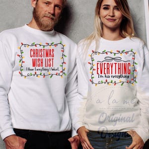 Puede incluir: Dos sudaderas blancas con texto navideño. Una dice "CHRISTMAS WISH LIST, I Have Everything I Want." La otra dice "EVERYTHING, I'm his everything." Ambas tienen un borde de luces festivo.