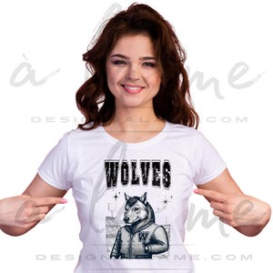 May include: White t-shirt featuring a graphic of a wolf wearing a letterman jacket with the letter "W". The word "WOLVES" is printed above the wolf illustration in a distressed font. The design includes stars and a stadium background.